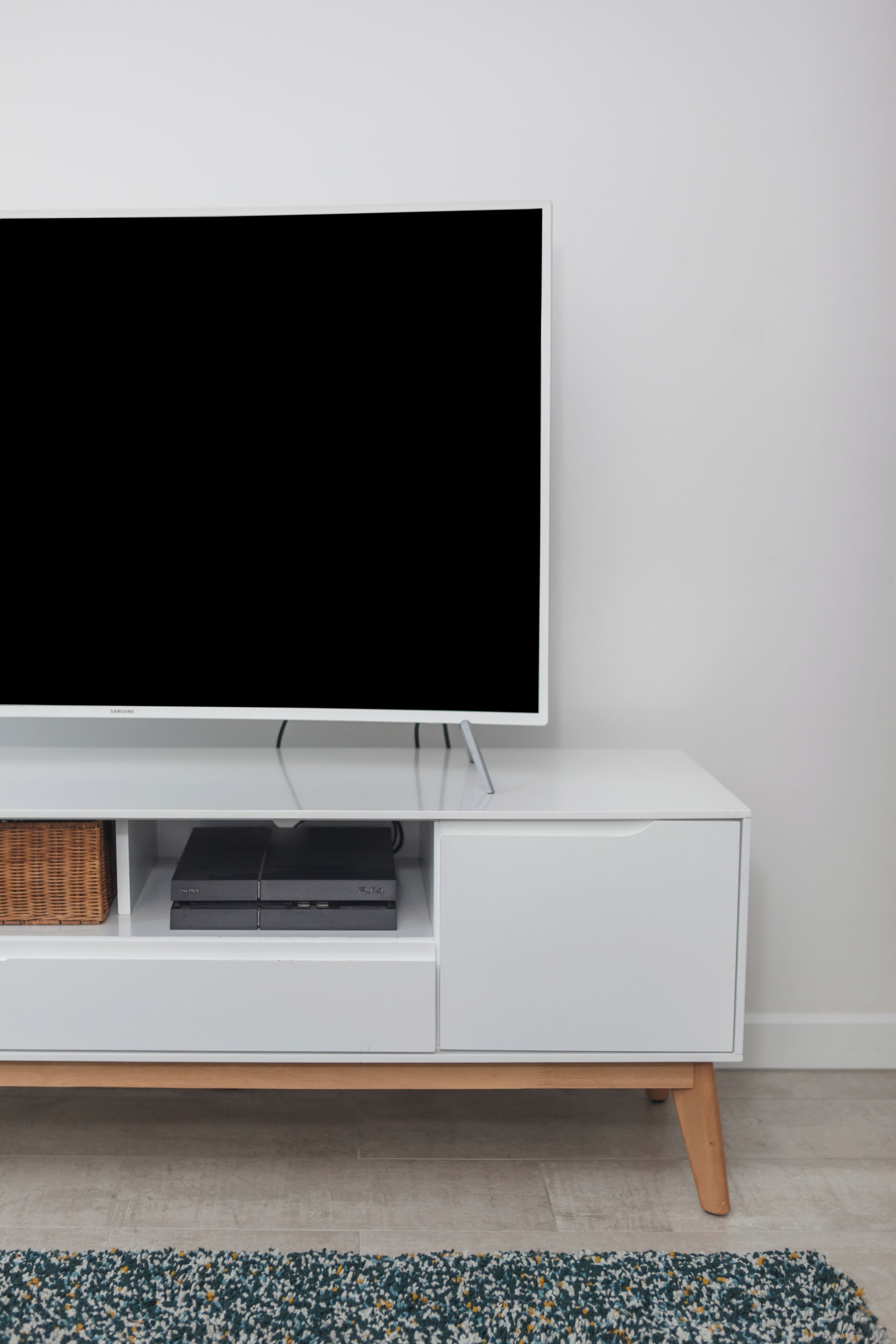 A white TV stand with a flat-screen TV, a black electronic device, and a woven basket.