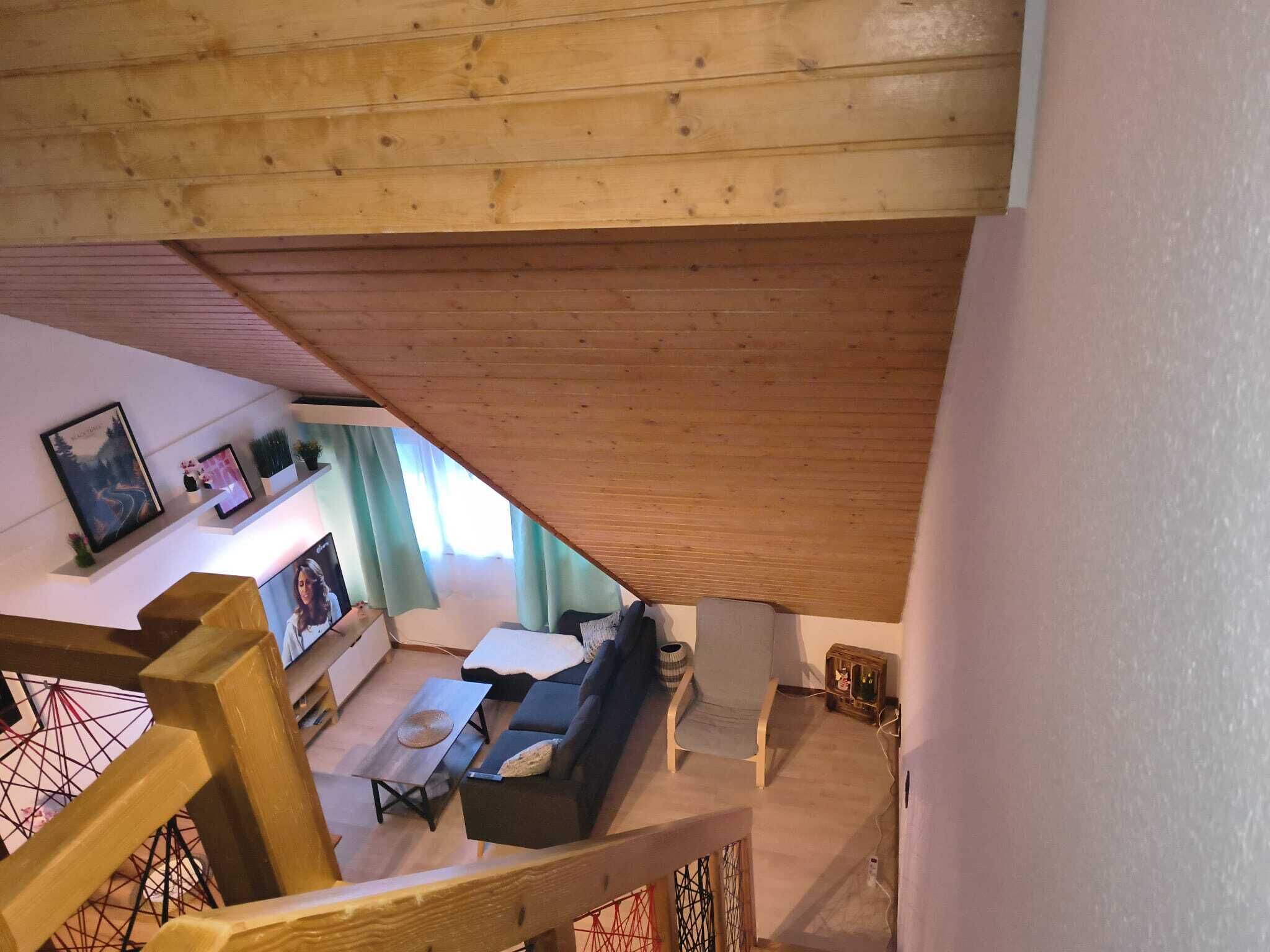 Een houten trap die leidt naar een leefruimte met een bank, een salontafel en een televisie.
