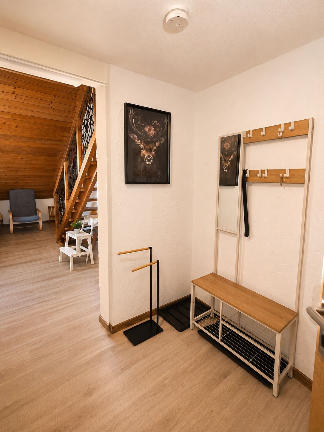 A room with a wooden staircase, a bench, a coat rack, and a framed deer artwork.