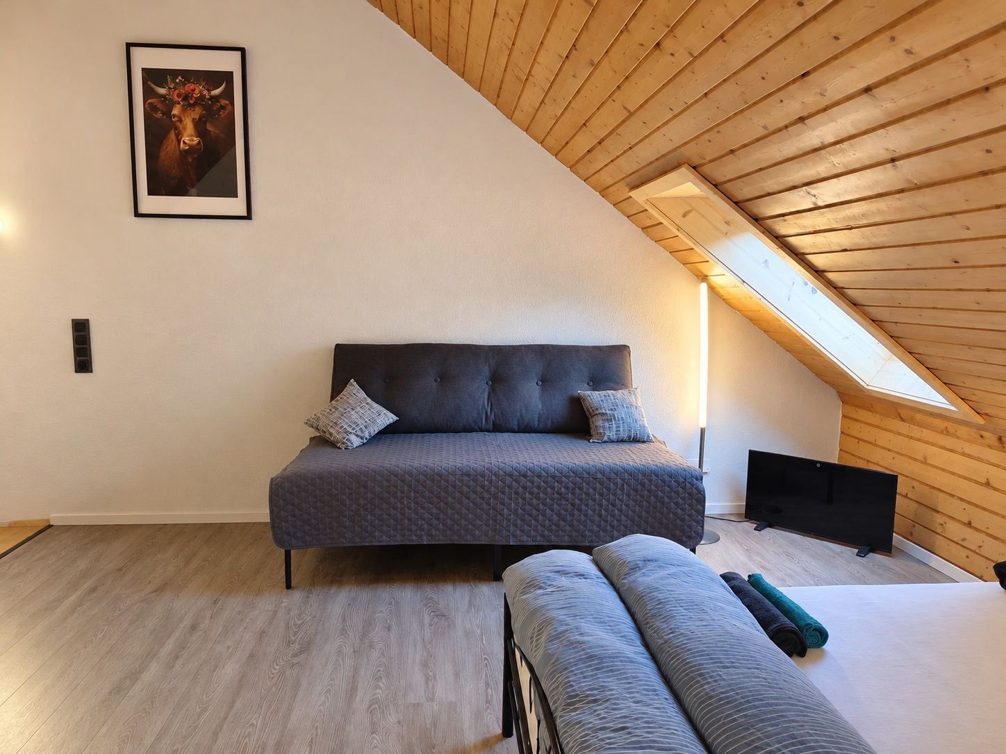 A bedroom with a sloped ceiling, a bed, a bench, and a framed picture on the wall.