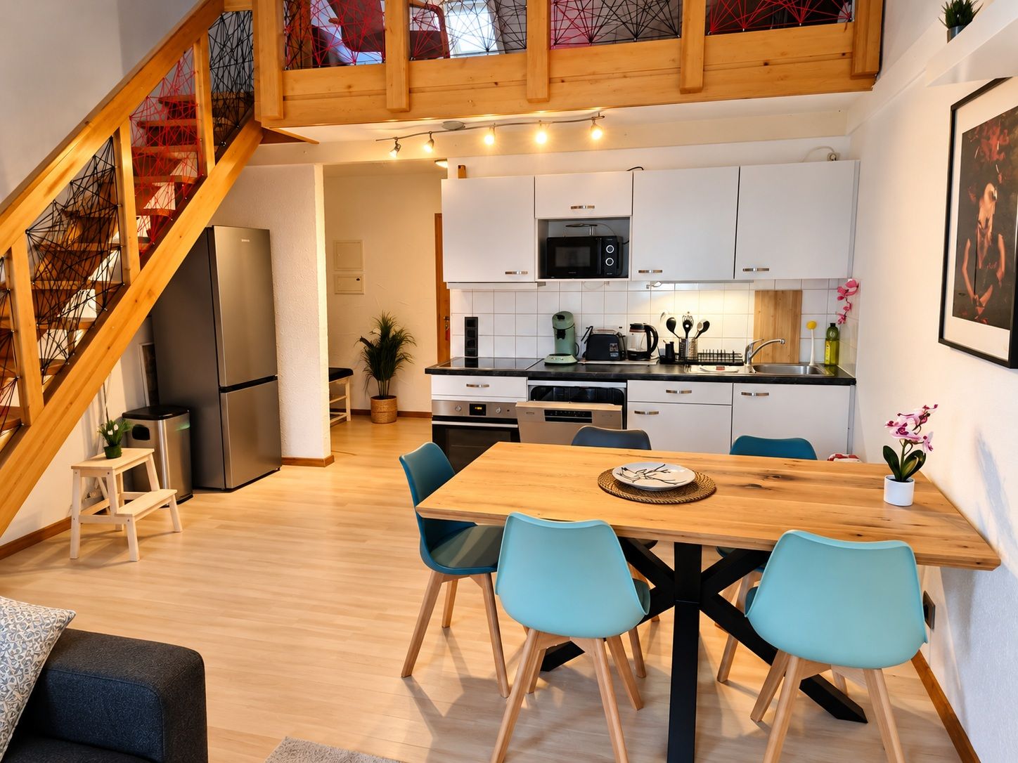 A modern kitchen with white cabinets, a microwave, and a dining area with a wooden table and blue chairs.