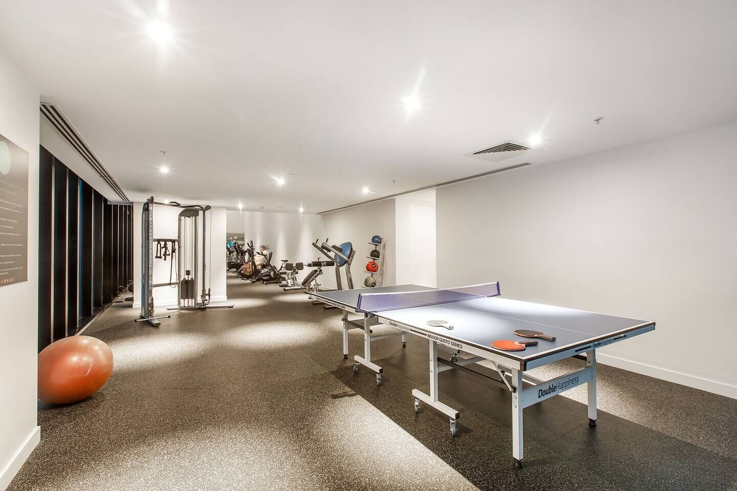 A gym with exercise equipment, a ping pong table, and a large exercise ball.