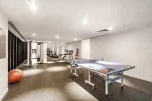 Une salle de sport équipée de matériel d’exercice, d’une table de ping-pong et d’un grand ballon de gymnastique.