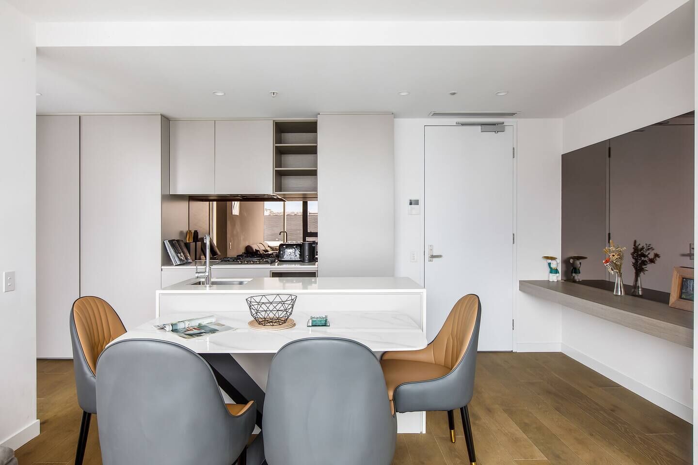 Une cuisine moderne avec des meubles blancs, une table à manger avec deux chaises et une cuisinière encastrée.