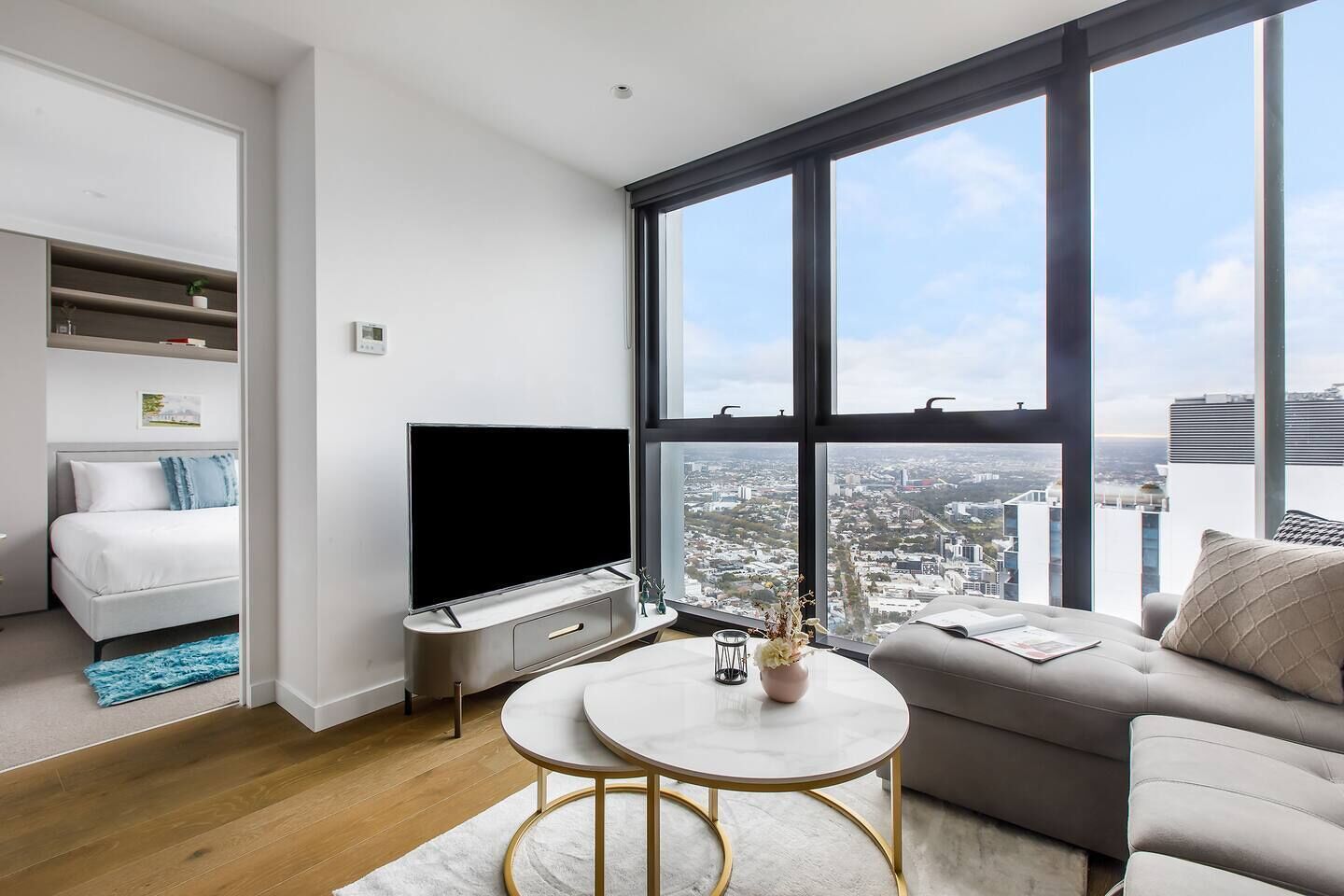 Ein modernes Wohnzimmer mit Fernseher, einer Couch, einem Couchtisch und Blick auf die Stadt durch große Fenster.