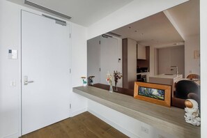 Un interior moderno con una puerta blanca, piso de madera, un espejo que refleja una cocina y una pequeña mesa con adornos.