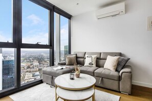Ein modernes Wohnzimmer mit einem grauen Sofa, einem runden Tisch und einem großen Fenster mit Blick auf die Stadt.