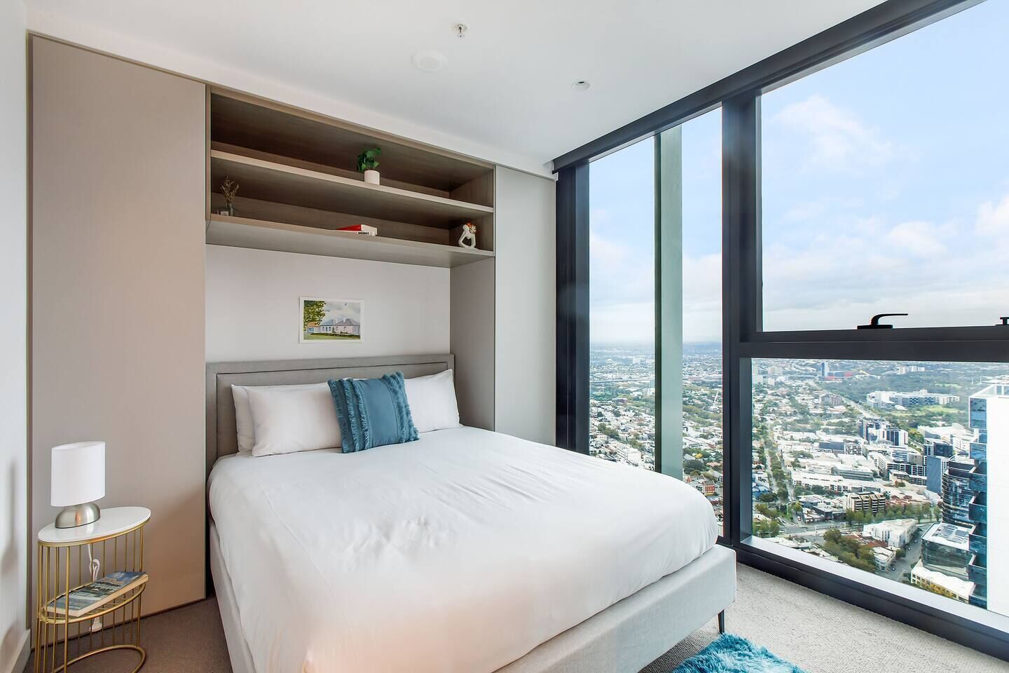 A modern hotel room with a large bed, a view of a cityscape, and built-in shelves with decorative items.