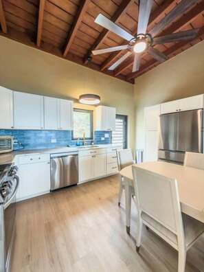 A kitchen with white cabinets, stainless steel appliances, a ceiling fan, and a window. - Sunset Sea-Clusion | Private Pool & Ocean Views (Frederiksted)