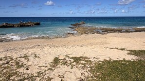 A beach with clear blue water, rocky outcrops, and sparse vegetation. - Sunset Sea-Clusion | Private Pool & Ocean Views (Frederiksted)