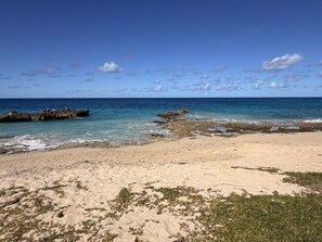 A beach with clear blue water, rocky outcrops, and sparse vegetation. - Sunset Sea-Clusion | Private Pool & Ocean Views (Frederiksted)