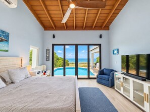 A bedroom with a bed, a TV, a sofa, and a view of a swimming pool and ocean. - Sunset Sea-Clusion | Private Pool & Ocean Views (Frederiksted)