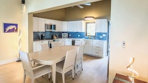 A modern kitchen with white cabinets, a dining table with chairs, and a small table with a lamp. - Sunset Sea-Clusion | Private Pool & Ocean Views (Frederiksted)