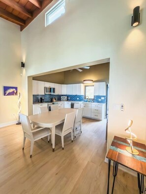 A modern kitchen with white cabinets, a dining table with chairs, and a small table with a lamp. - Sunset Sea-Clusion | Private Pool & Ocean Views (Frederiksted)