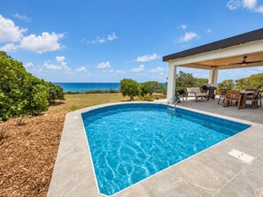 A rectangular swimming pool with a clear blue water surface, surrounded by a stone deck.