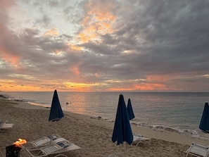 A beach with umbrellas and lounge chairs, a sunset, and the ocean.