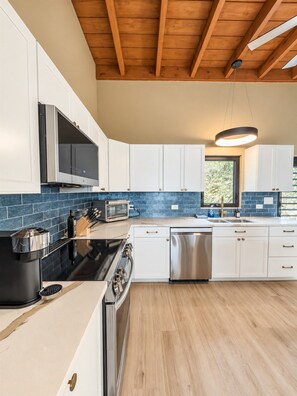 A modern kitchen with white cabinets, a black stove, stainless steel appliances, and a blue-tiled backsplash.
