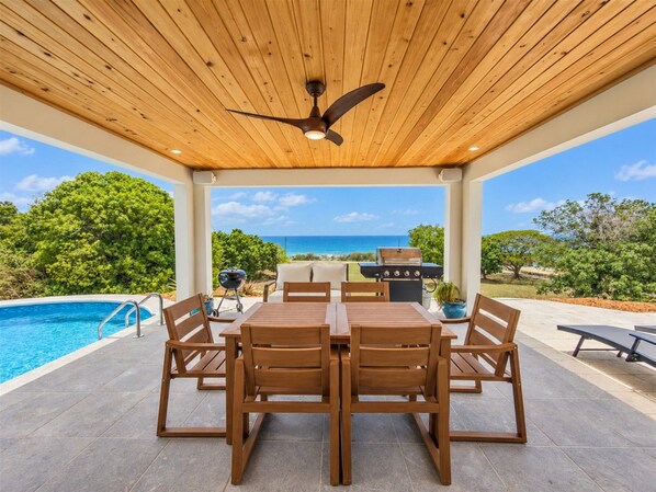 An outdoor patio with a pool, wooden furniture, and a view of the ocean.