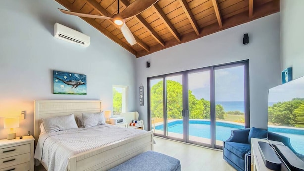 A bedroom with a bed, a desk, and a view of a swimming pool. - Sunset Sea-Clusion | Private Pool & Ocean Views (Frederiksted)