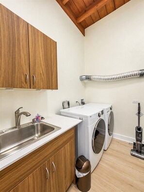 A laundry room with a sink, two washing machines, and a vacuum cleaner. - Sunset Sea-Clusion | Private Pool & Ocean Views (Frederiksted)