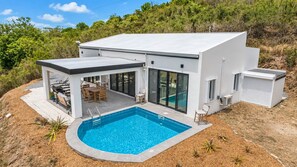 A modern house with a swimming pool, outdoor seating, and a covered patio.