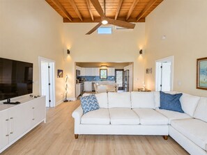 A spacious living room with a white sofa, a television, and a ceiling fan.