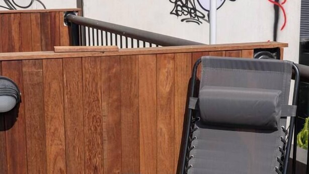 A black lounge chair with a cushion, positioned on a wooden deck with a magazine on the table. - Noir Haven Stylish CBD Escape with Private Rooftop (Melbourne)