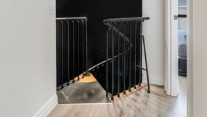 A staircase with a black railing, a light fixture above, and a door leading to another room. - Noir Haven Stylish CBD Escape with Private Rooftop (Melbourne)