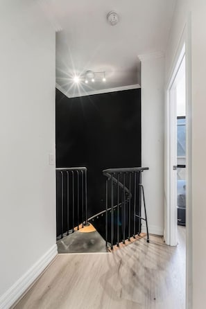 A staircase with a black railing, a light fixture above, and a door leading to another room. - Noir Haven Stylish CBD Escape with Private Rooftop (Melbourne)
