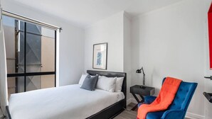 A modern bedroom with a bed, a chair, a nightstand, and a window. - Noir Haven Stylish CBD Escape with Private Rooftop (Melbourne)