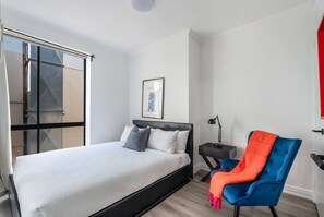 A modern bedroom with a bed, a chair, a nightstand, and a window. - Noir Haven Stylish CBD Escape with Private Rooftop (Melbourne)
