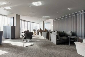 Un hall d’hôtel moderne doté d’un espace salon, d’un comptoir d’accueil et d’une grande fenêtre laissant entrer la lumière naturelle.