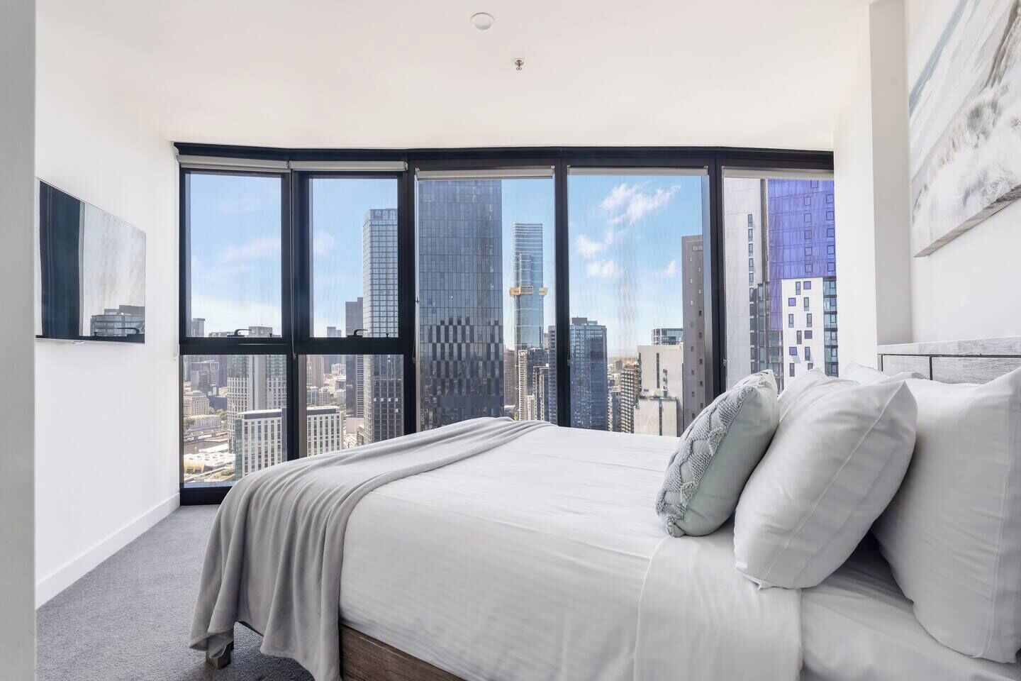 A bedroom with a large bed, a view of the cityscape through floor-to-ceiling windows, and a modern design.