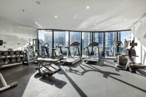 A modern gym with treadmills, dumbbells, and exercise equipment, featuring large windows with a city view. - Skyline 40 Southbank Made Easy with Pool and Gym (Southbank)