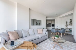A modern living room with a grey sofa, a glass coffee table, and a dining area with chairs. - Skyline 40 Southbank Made Easy with Pool and Gym (Southbank)