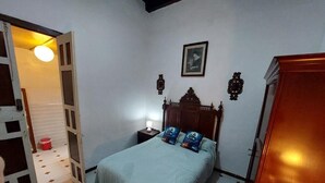 A bedroom with a bed, a nightstand, a wooden wardrobe, and a door leading to another room.