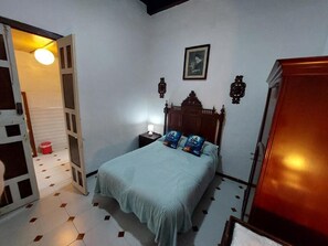 Un dormitorio con cama, mesita de noche, armario de madera y una puerta que da a otra habitación.