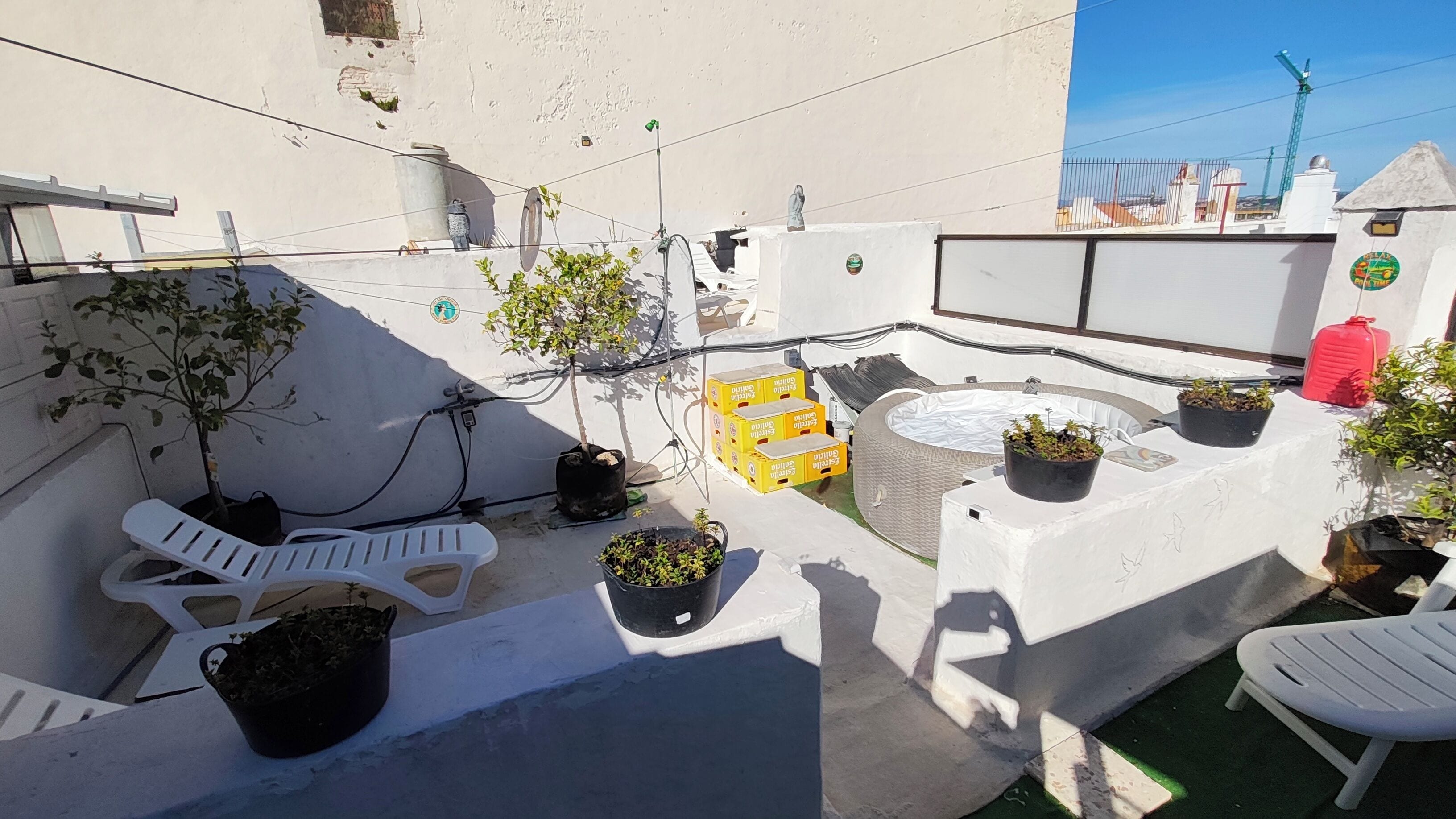 A rooftop terrace with white plastic chairs, potted plants, and a small pool.