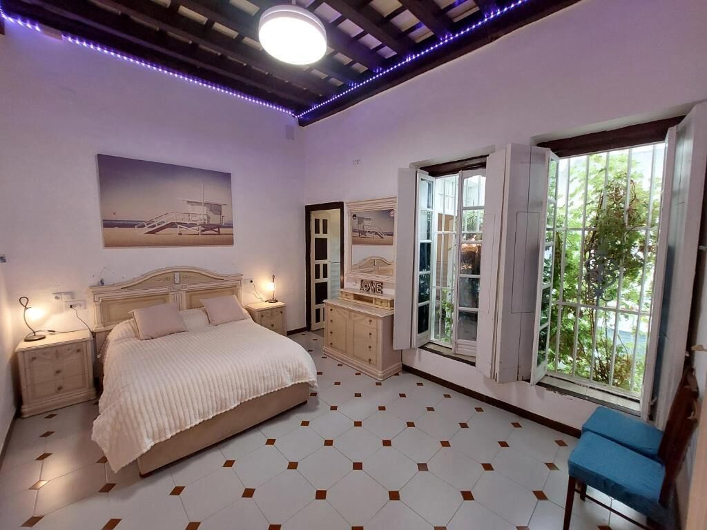 A bedroom with a bed, bedside tables, a dresser, a window with a view, and a ceiling with exposed beams and lighting.