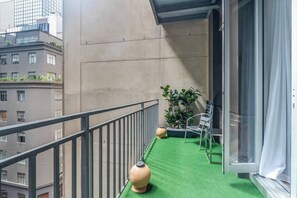 A balcony with a green artificial turf, two potted plants, and a metal railing. - Urban Rest Simple CBD Escape with Gym and Sauna (Melbourne)