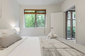 Een slaapkamer met een bed, een raam met uitzicht op groen en een deur naar een balkon.