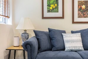 A grey sofa with multiple cushions, a table lamp, and framed botanical prints on the wall. - Experience the St Kilda Vibe from a Cosy Retreat (Saint Kilda)