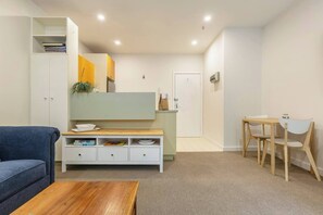A modern living room with a sofa, a wooden coffee table, a TV stand, and a dining area with a table and chairs. - Experience the St Kilda Vibe from a Cosy Retreat (Saint Kilda)