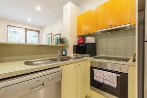 A modern kitchen with a dishwasher, microwave, oven, and wooden cabinets. - Experience the St Kilda Vibe from a Cosy Retreat (Saint Kilda)