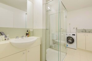 Een moderne badkamer met een douchecabine van glas, een wastafel met toiletartikelen en een wasmachine.