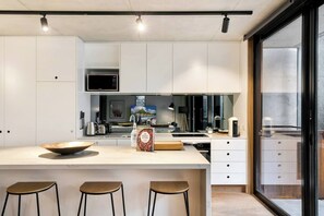 Une cuisine moderne avec des meubles blancs, un grand îlot central doté de tabourets, un four à micro-ondes et une machine à café.