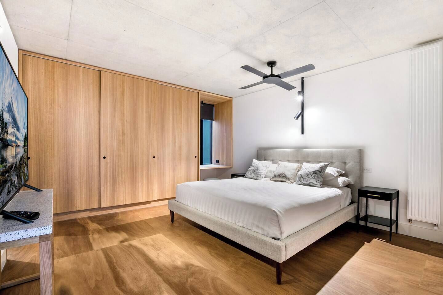 A bedroom with a bed, a ceiling fan, a wardrobe, and a TV on a stand.