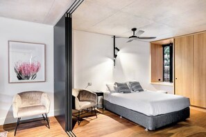 Une chambre moderne comprenant un lit, deux chaises, un bureau, un ventilateur de plafond et une fenêtre donnant sur un beau paysage.