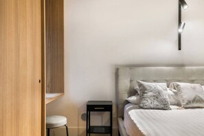 Een slaapkamer met een bed, nachtkastje, stoel en een houten garderobe.