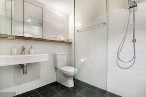 Een moderne badkamer met een douchecabine van glas, een wit toilet en een wastafel met een houten plank erboven.